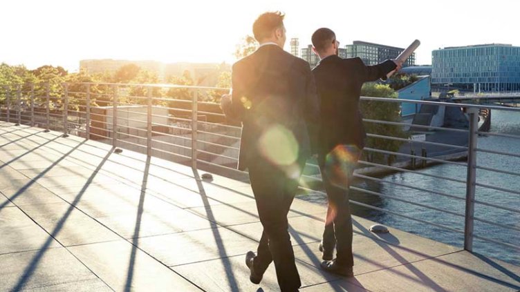 Two businessmen walking on a bridge by the river