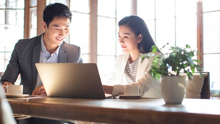 Two professionals smiling and working on new strategies using a laptop while sitting in the office workplace