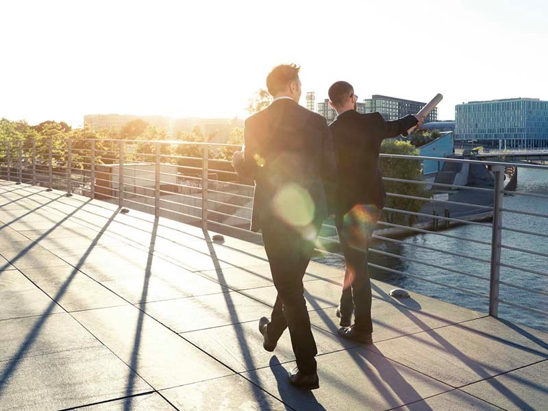 Two businessmen walking on a bridge by the river