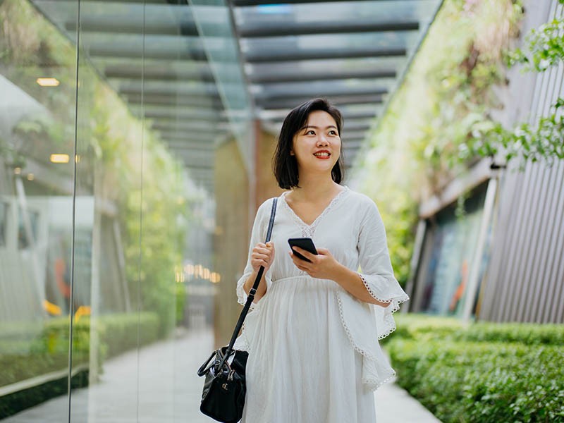 a smiling woman holding smartphone and looking away in a green building