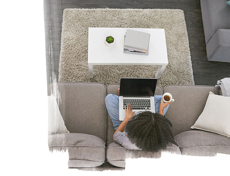 High angle shot of a young woman using a laptop and having coffee on the sofa at home